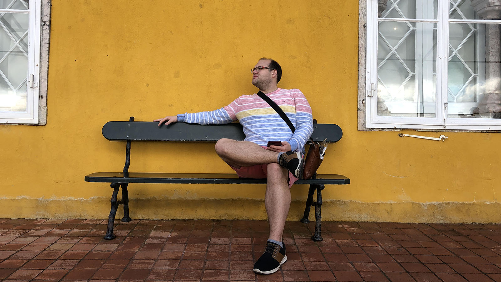 Composer Cameron Wentz sitting on a bench against a yellow-painted wall.