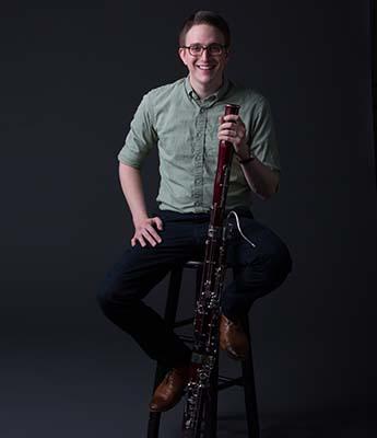 William Short sitting on a stool and holding his bassoon.